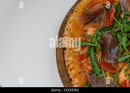 Pizza pepperoni avec roquette et prosciutto. Pizza à la viande avec fromage, tomates cerises et roquette fraîche sur un stand en bois Banque D'Images