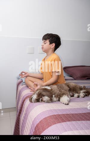 Garçon brésilien de 11 ans assis sur son lit, pratiquant le yoga à côté de son chien 3. Banque D'Images