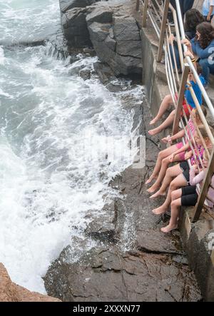 Les enfants apprécient le frisson des vagues qui s'écrasent haut sur les rochers du parc national Acadia après que l'ouragan Ernesto a déferlé sur les eaux. Banque D'Images