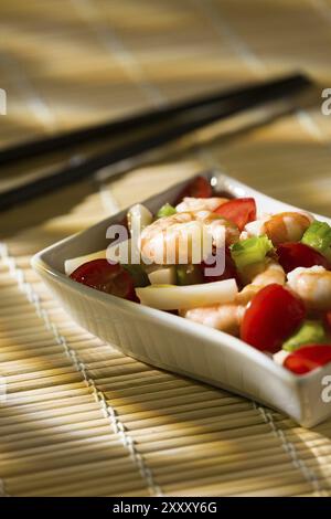 Salade de crevettes avec céleri de tomates calmars dans un bol blanc sur une nappe de bambou et des baguettes Banque D'Images