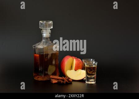 Liqueur de pomme à la cannelle et à l'anis, alcool maison fort dans deux verres et une bouteille sur fond noir. Gros plan. Banque D'Images
