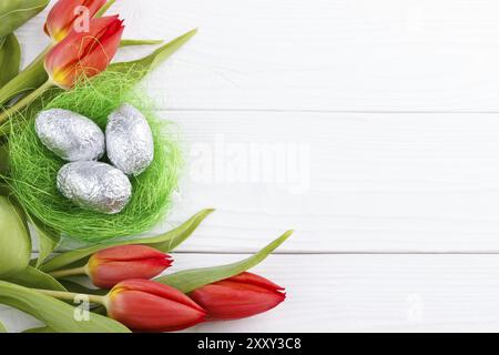 Tulipes rouges et oeufs dans un nid sur planche de bois blanc, fond de Pâques Banque D'Images