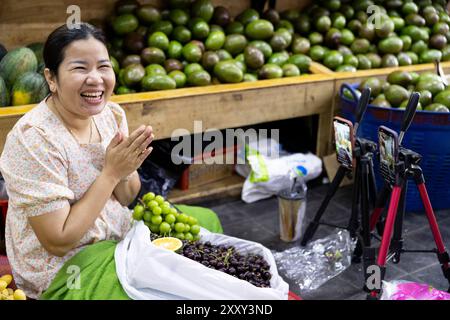 Une joyeuse vendeuse de fruits diffusant en direct ses produits, y compris des cerises, des oranges et des avocats, sur un marché de Phnom Penh, au Cambodge. Banque D'Images