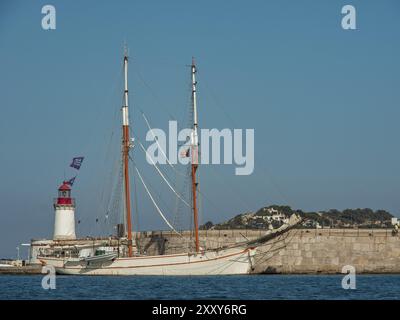 Voilier à côté d'un phare dans le port avec un mur de pierre et mer calme sous un ciel bleu clair, ibiza, mer méditerranée, espagne Banque D'Images