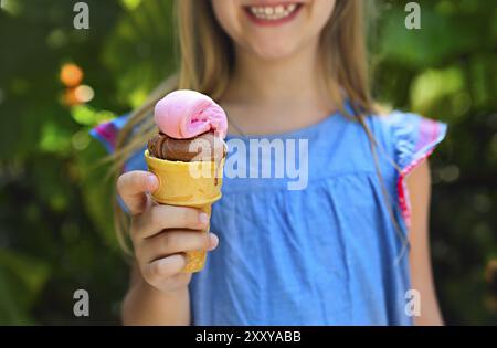 Cute little girl avec expression drole holding ice cream cone à l'extérieur contre nature fond lumineux. Close up Banque D'Images