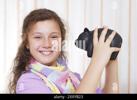 Petite fille économisant de l'argent dans une tirelire. Portrait en intérieur Banque D'Images