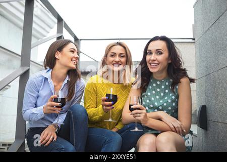 Trois jeunes femmes heureuses riant, buvant du vin rouge, s'amusant. Concept de fête et d'amitié Banque D'Images