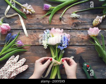 Un fleuriste au travail. Femme faisant bouquet de fleurs de printemps sur la table en bois rustique Banque D'Images