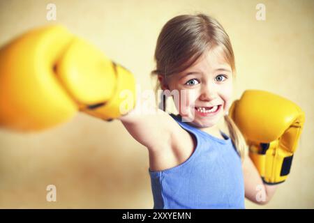 Petite fille aux gants de boxe jaune sur jaune wall background. Girl power concept. Funny little kid portrait. Heureux dent perdue petite fille portrai Banque D'Images