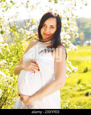 Magnifique Portrait de femme enceinte en robe blanche dans le parc printemps floraison Banque D'Images