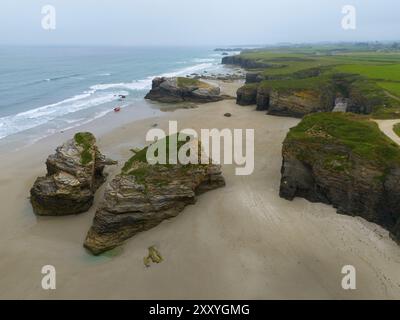 Large plage avec de grandes formations rocheuses dispersées et de l'eau calme, bordée par des falaises côtières abruptes, vue aérienne, Praia das Catedrais, Playa de las Cated Banque D'Images