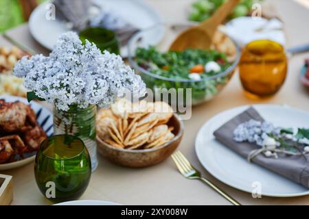 Table bien agencée avec une variété de plats frais, des salades vibrantes, des collations et des fleurs décoratives créant une atmosphère chaleureuse et accueillante pour pique-niquer en plein air Banque D'Images