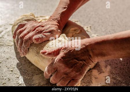 La préparation des pâtes aux mains des femmes. Faire de la pâte par des mains masculines à la boulangerie. Pâte à main. Mains féminines fabriquant de la pâte pour pizza. Pâte de cuisson pour pain et Banque D'Images
