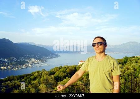 Touriste souriant debout sur fond d'une belle vue sur la baie de Kotor. Portrait d'un homme se relaxant sur la côte du Monténégro. Banque D'Images