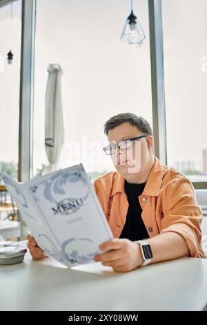 Un homme atteint du syndrome de Down est assis à une table de café, lisant soigneusement le menu. Banque D'Images