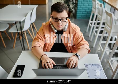 Un homme atteint du syndrome de Down est assis à une table de café, concentré sur son ordinateur portable. Banque D'Images