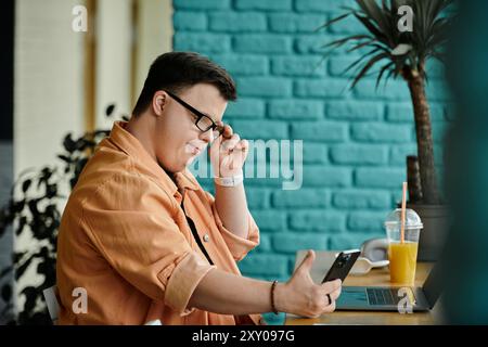 Un homme atteint du syndrome de Down est assis à une table dans un café, travaillant sur son ordinateur portable. Banque D'Images