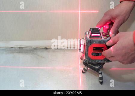 Niveau laser de construction et les mains d'un ouvrier. Le constructeur mesure le niveau. Concept de réparation Banque D'Images