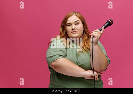 Une femme dans une chemise verte tient en toute confiance un microphone sur un fond rose. Banque D'Images