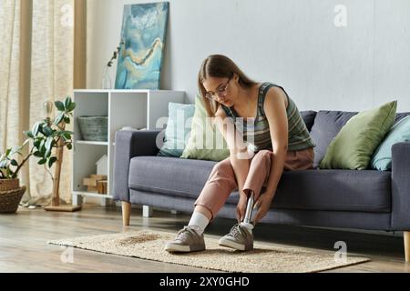 Une jeune femme est assise sur un canapé dans son salon, ajustant la prothèse de jambe qu'elle porte. Banque D'Images