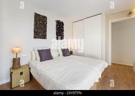 Une chambre contemporaine avec deux lits simples avec literie neutre, art mural unique au-dessus, parquet, et une armoire intégrée cette configuration comprend Banque D'Images