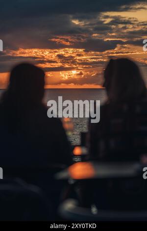 Silhouettes de deux personnes profitant d'un dîner pittoresque contre un coucher de soleil spectaculaire sur l'océan aux Açores, soulignant un moment serein et romantique Banque D'Images