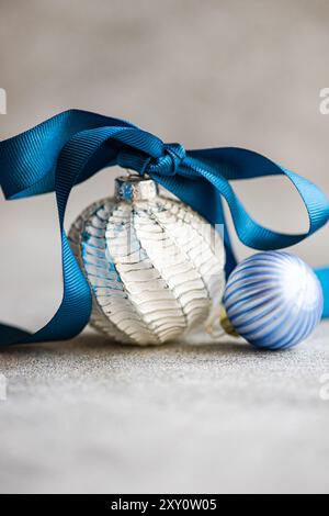 Gros plan de décorations de Noël étincelantes avec un ruban de satin bleu, placé sur un fond de béton texturé pour un contraste d'eleme doux et dur Banque D'Images