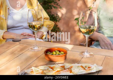 Vue recadrée méconnaissable de deux femmes profitant du temps libre avec du vin et des collations sur une table en bois à l'extérieur. Olives et fromage en tranches complètent th Banque D'Images