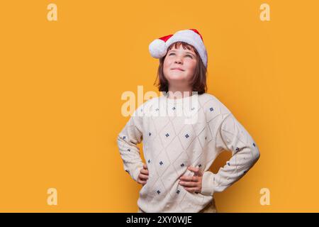 Une jeune fille de preteen joyeuse portant un chapeau de Père Noël regarde vers le haut avec un large sourire, placé sur un fond jaune Uni. Banque D'Images