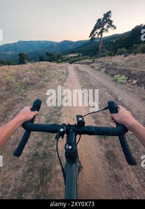 Perspective à la première personne recadrée et méconnaissable du cyclisme sur un vélo de gravier le long d'un sentier poussiéreux au milieu d'un terrain montagneux. Les bras du cavalier et le t Banque D'Images