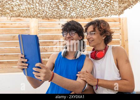 Un couple gay heureux profite d'une journée ensoleillée ensemble, partageant du contenu sur une tablette numérique sous un patio ombragé, reflétant un lien chaleureux et tranquille Banque D'Images