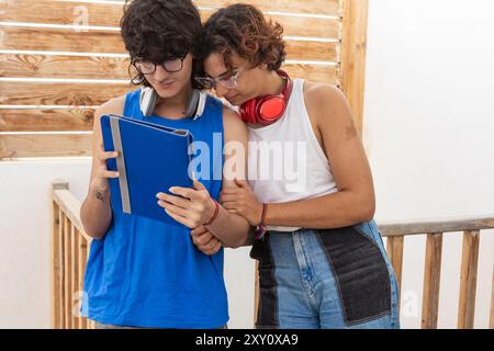 Un couple gay heureux profite d'une journée ensoleillée ensemble, partageant du contenu sur une tablette numérique sous un patio ombragé, reflétant un lien chaleureux et tranquille Banque D'Images