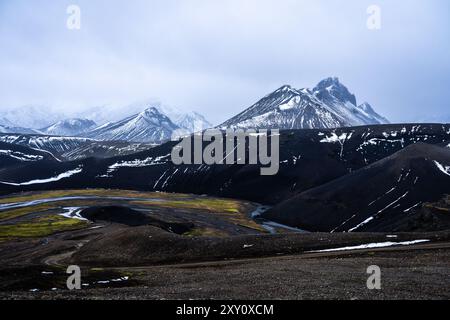 Un paysage saisissant en Islande avec des montagnes sombres et escarpées partiellement couvertes de neige, avec des vallées verdoyantes et des rivières sinueuses sous la scène Banque D'Images