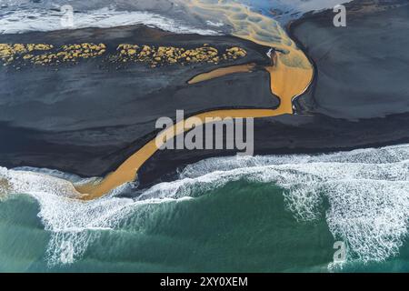 Vue de dessus capturant l'endroit où la rivière Holtsos, avec son limon doré distinct, se fond harmonieusement dans l'océan le long de la côte accidentée de l'Islande, accentua Banque D'Images