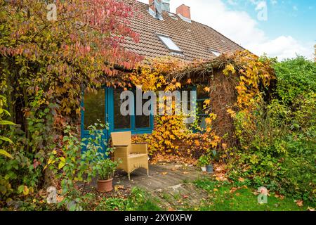 Charmante maison de campagne enveloppée de feuilles d'automne vibrantes, avec un porche en bois pittoresque. Banque D'Images