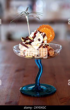 Un sundae de crème glacée décadent avec plusieurs cuillères ornées de crème fouettée, de copeaux de chocolat et d'un délicat biscuit gaufré dans un élégant bleu Banque D'Images