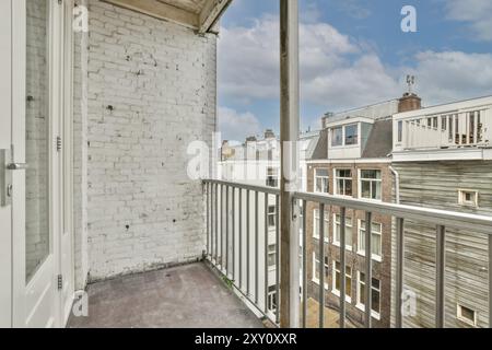 Un balcon urbain confortable avec un mur de briques peintes en blanc, balustrade en fer et une vue panoramique sur les toits de la ville sous un ciel bleu clair. Banque D'Images