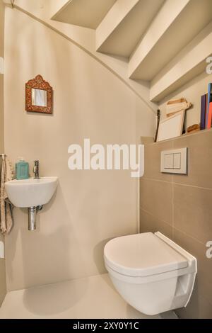 Un coin compact et bien organisé dans une salle de bains moderne avec des toilettes en céramique blanche et un lavabo, sous un plafond incliné avec poutres. Banque D'Images