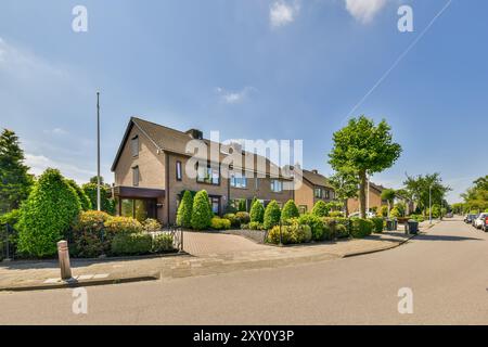 Une rue de banlieue calme présente une rangée de maisons mitoyennes contemporaines avec des jardins bien entretenus sous un ciel bleu vif. Banque D'Images