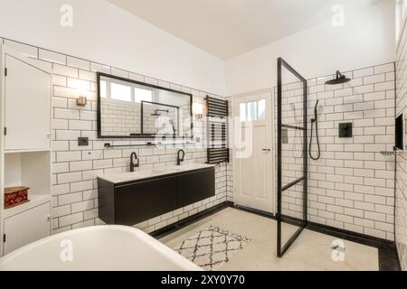 Une salle de bains contemporaine dotée d'une douche à l'italienne, de carreaux blancs de métro et de luminaires noirs étincelants de propreté et de style. Banque D'Images