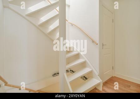 Une image d'un escalier blanc moderne et lumineux avec une main courante en bois, menant à une porte fermée dans un espace bien éclairé. Banque D'Images