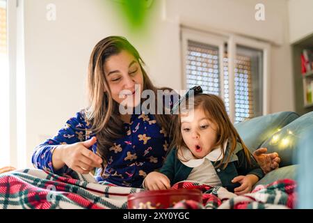 Une scène réconfortante d'une mère et d'une fille partageant un moment joyeux à Noël à la maison, avec des décorations festives autour d'elles Banque D'Images