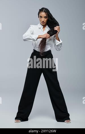 Femme afro-américaine confiante pose avec des cheveux et une chemise blanche devant un fond gris Banque D'Images