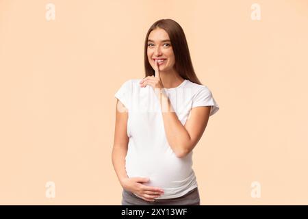 Joyeuse fille enceinte Gesturing collés sur des lèvres Standing, Studio Shot Banque D'Images