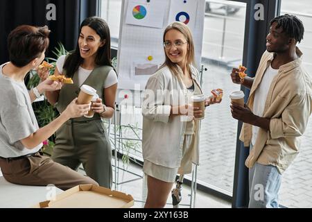 Quatre collègues profitent d'une pause déjeuner décontractée avec pizza et café. Banque D'Images