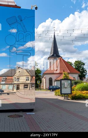 Tukums, Lettonie - 22 août 2024 : une église se dresse à côté d'une installation moderne réfléchissante à la lumière du soleil. Banque D'Images