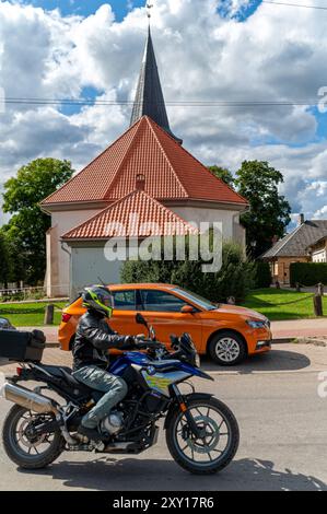 Tukums, Lettonie - 22 août 2024 : un motocycliste passe devant un bâtiment d'église à l'architecture unique. Banque D'Images