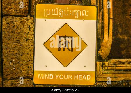 Affiche bilingue « Mind Your Head ». Temple Banteay Srei, parc archéologique d'Angkor, province de Siem Reap, Cambodge. © Brooks Lieb Banque D'Images