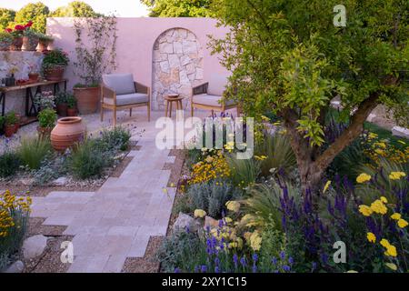 Un mur de calcaire derrière une terrasse pavée et un chemin entouré de plantes tolérantes à la sécheresse dans le jardin Meditrraneo. Designer : Katerina Kanatali Banque D'Images