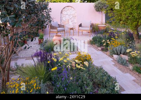 Un mur de calcaire derrière une terrasse pavée et un chemin entouré de plantes tolérantes à la sécheresse, y compris Achillea 'Moonshine', Salvia nemerosa 'Carado Banque D'Images